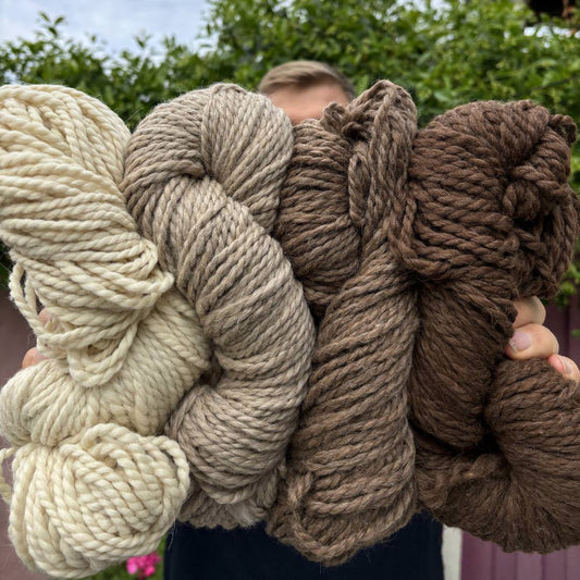 Four soft llama yarns in vibrant colors held in a man's hand, showcasing the yarn's texture and richness, perfect for various knitting and crafting projects.